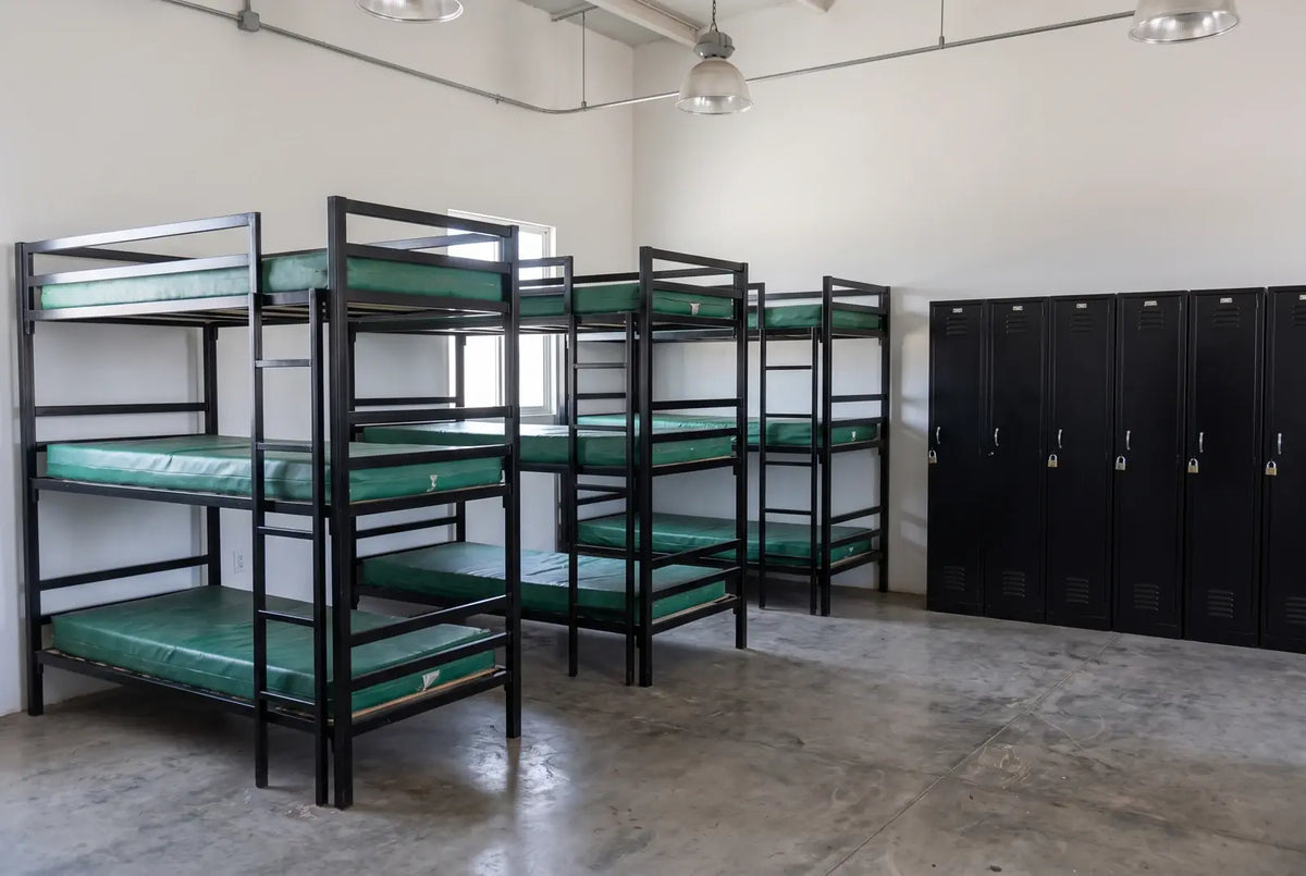 Dormitorio de campamento con literas triples, colchonetas y lockers